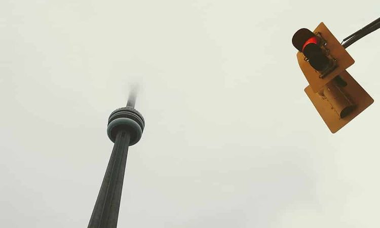 CN Tower shrouded in fog, with a red traffic light in the foreground against a gray sky.