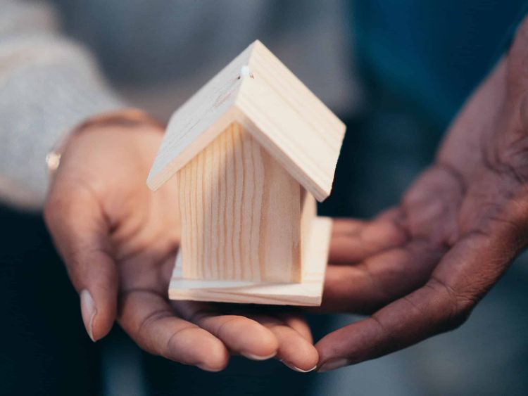 Close-up of a pair of hands cradling a miniature wooden house.