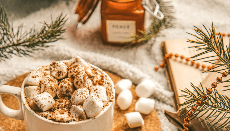 Cozy hot chocolate with marshmallows, pine branches, a "PEACE" candle, and festive beads.