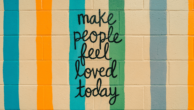 Colorful striped brick wall with black script: "make people feel loved today".