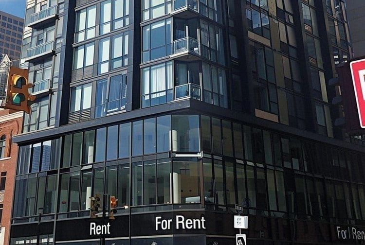Street-level view of a modern glass building with multiple "For Rent" signs on the ground floor.