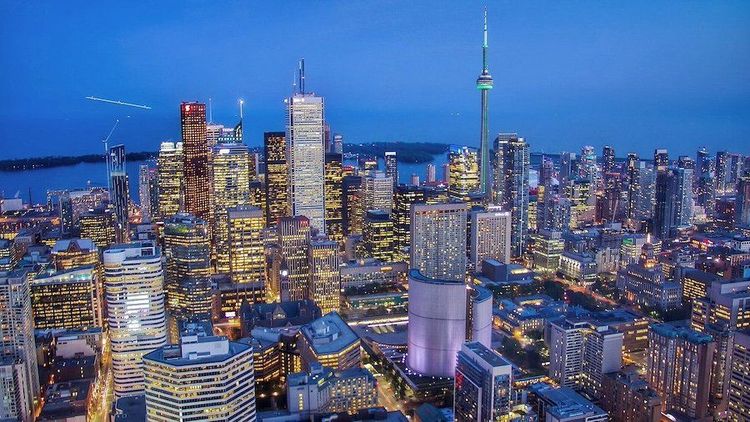 Aerial view of the Toronto city skyline at dusk, with numerous illuminated skyscrapers and the CN Tower.